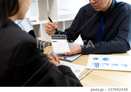 Coach pointing at calculator and paper graph chart to teach young businesswoman 137942439