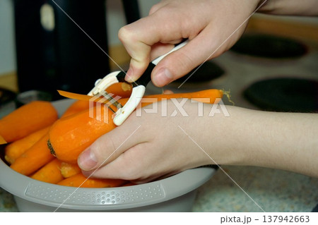 Woman hands peeling a fresh carrot with a peeler over a bowl. Woman hands peeling a fresh carrot with a peeler over a bowl. 137942663