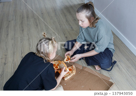 Lovely young children sitting on floor in living room and eating pizza at home 137943050