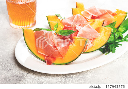 Cantaloupe melon with prosciutto and fresh basil, on a white plate, natural light, 137943276