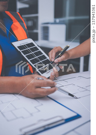 engineer and an architect reviewing blueprints and construction plans together at a bustling construction site 137943361