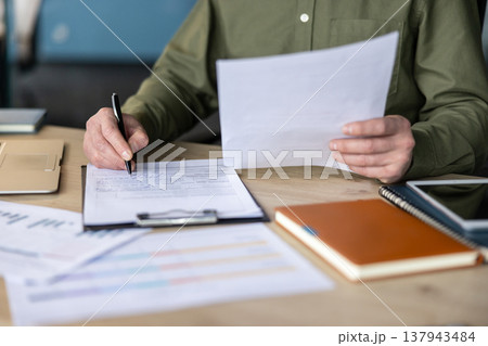Person's hands signing a legal contract or important business document, demonstrating agreement, paperwork, and financial management in an office setting 137943484