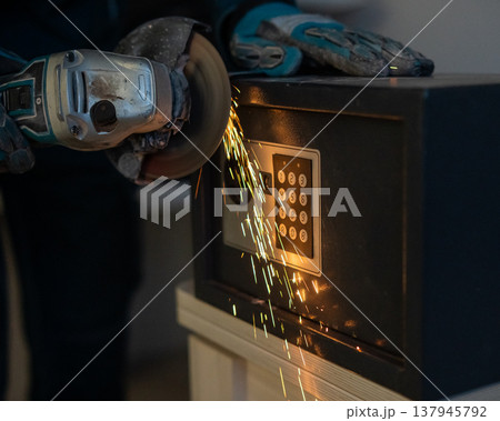 A man breaks into a safe with a grinder. 137945792