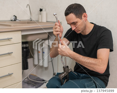 A plumber is replacing a faucet in the kitchen. 137945899