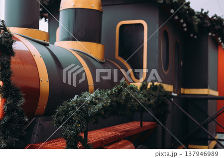 Decorative Christmas steam train decorated with pine garlands and lights at a holiday market. Festive winter background. Vintage transportation. Decorative Christmas steam train decorated with pine garlands and lights at a holiday market. Festive winter background. Vintage transportation. 137946989
