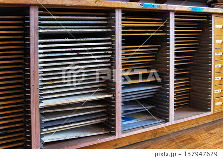 A closeup of wooden drying racks filled with stacked artwork and drawing boards in a studio setting. labeled storage compartments A closeup of wooden drying racks filled with stacked artwork and drawing boards in a studio setting. labeled storage compartments 137947629