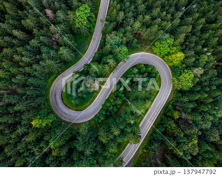 Top down aerial view of a curving mountain road with sharp hairpin turns surrounded by dense green conifer forest in a scenic natural landscape. Top down aerial view of a curving mountain road with sharp hairpin turns surrounded by dense green conifer forest in a scenic natural landscape. 137947792