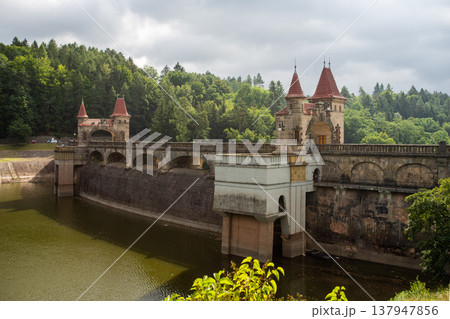 Historic Les Kralovstvi dam with stone towers and bridge above reservoir surrounded by forest in Czech Republic Historic Les Kralovstvi dam with stone towers and bridge above reservoir surrounded by forest in Czech Republic 137947856