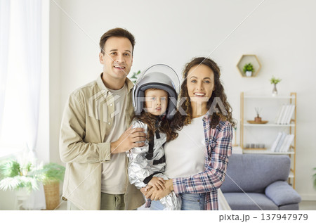 Parents and daughter in astronaut costume smiling together in cozy living room 137947979