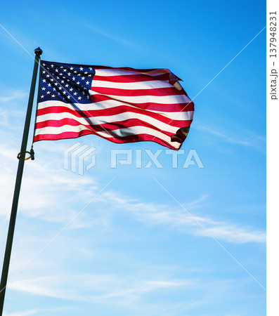 Flag of United States waving on a pole against a clear blue sky.  American flag with stars and stripesv 137948231