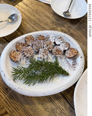Dessert plate with pine nut grillage pieces dusted with powdered sugar and decorated with spruce branch on wooden table in restaurant setting under warm light. Dessert presentation, menu content Dessert plate with pine nut grillage pieces dusted with powdered sugar and decorated with spruce branch on wooden table in restaurant setting under warm light. Dessert presentation, menu content 137948398