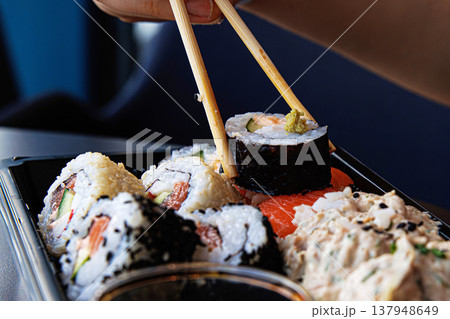 Chopsticks grasping sushi roll with cucumber, avocade and salmon. Maki being picked up with chopsticks. Selective focus Chopsticks grasping sushi roll with cucumber, avocade and salmon. Maki being picked up with chopsticks. Selective focus 137948649