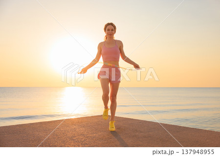Fit woman jumping rope at the beach during summer vacation Fit woman jumping rope at the beach during summer vacation 137948955