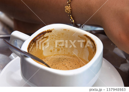 Finished espresso cup with coffee stains and spoon on a metal cafe table. Young woman arm in the background. Selective focus Finished espresso cup with coffee stains and spoon on a metal cafe table. Young woman arm in the background. Selective focus 137948983