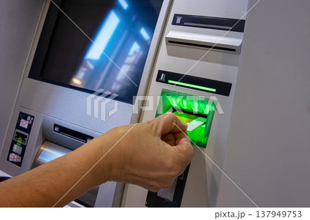 ATM Card Entering Illuminated Slot. Cash machine card reader slot glowing green as a card is inserted by person hand. ATM Card Entering Illuminated Slot. Cash machine card reader slot glowing green as a card is inserted by person hand. 137949753