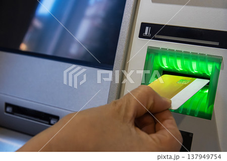 ATM Card Entering Illuminated Slot. Cash machine card reader slot glowing green as a card is inserted by person hand. ATM Card Entering Illuminated Slot. Cash machine card reader slot glowing green as a card is inserted by person hand. 137949754
