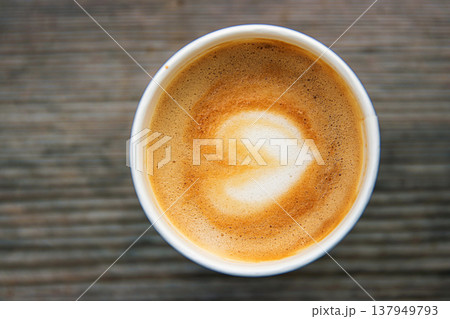 Top down view of a paper coffee cup, placed on a rustic wooden table, filled with a creamy latte featuring heart shaped latte art Top down view of a paper coffee cup, placed on a rustic wooden table, filled with a creamy latte featuring heart shaped latte art 137949793