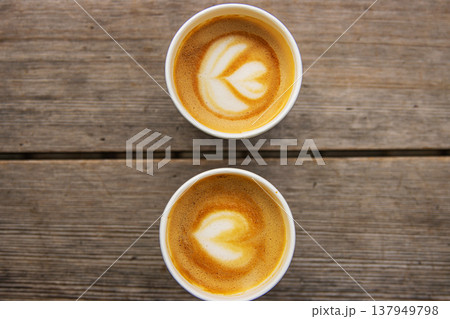 Top down view of two paper coffee cups, placed on a rustic wooden table, with a creamy heart and flower shaped latte art Top down view of two paper coffee cups, placed on a rustic wooden table, with a creamy heart and flower shaped latte art 137949798