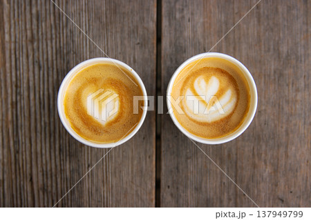 Top down view of two paper coffee cups, placed on a rustic wooden table, with a creamy heart and flower shaped latte art Top down view of two paper coffee cups, placed on a rustic wooden table, with a creamy heart and flower shaped latte art 137949799