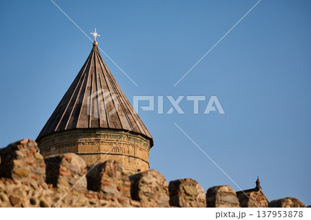 Traditional Georgian Orthodox church tower with conical roof above a textured stone wall 137953878