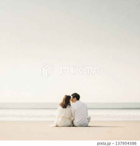 青空の下の砂浜に座ってキスをする男女の若いカップル 137954386