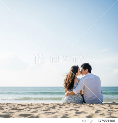 青空の下の砂浜に座ってキスをする男女の若いカップル 137954406