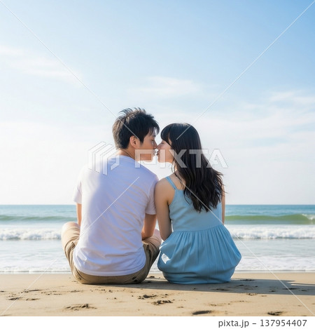 青空の下の砂浜に座ってキスをする男女の若いカップル 137954407