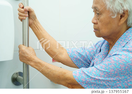 Asian elderly woman patient use toilet support rail in bathroom. Asian elderly woman patient use toilet support rail in bathroom. 137955167