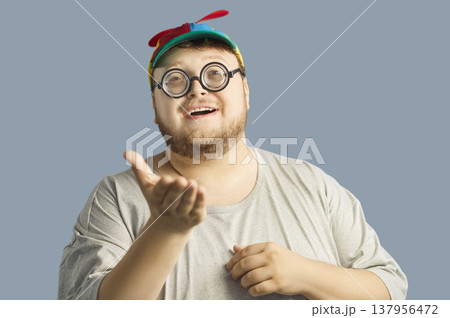 Smiling chubby man in propeller beanie and glasses, inviting gesture, studio 137956472