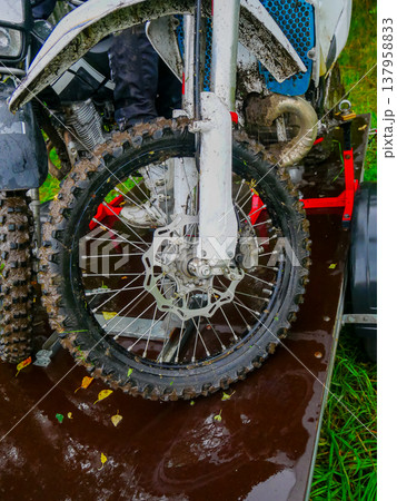 Muddy front wheel of a dirt bike secured on a trailer. Extreme sports motorcycle after off-road competition. Motocross motorcycle on transportation rack for travel and adventure. Muddy front wheel of a dirt bike secured on a trailer. Extreme sports motorcycle after off-road competition. Motocross motorcycle on transportation rack for travel and adventure. 137958833