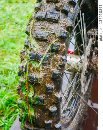 Muddy motorcycle tire on nature trail. Dirty motocross wheel covered in clay after riding off-road. Extreme sports adventure concept. Rough terrain travel and active leisure lifestyle. 137958841