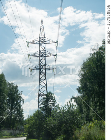 Power transmission tower standing in nature. High voltage electrical pylon with cables against blue sky. Infrastructure grid for electrical power supply, distribution and utility delivery. Power transmission tower standing in nature. High voltage electrical pylon with cables against blue sky. Infrastructure grid for electrical power supply, distribution and utility delivery. 137958856