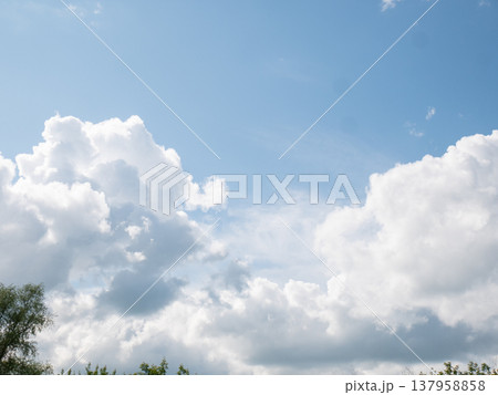 White fluffy clouds against clear blue sky. Nature background landscape with horizon trees. Weather and climate concept for environmental awareness and peaceful atmosphere in daily life. White fluffy clouds against clear blue sky. Nature background landscape with horizon trees. Weather and climate concept for environmental awareness and peaceful atmosphere in daily life. 137958858