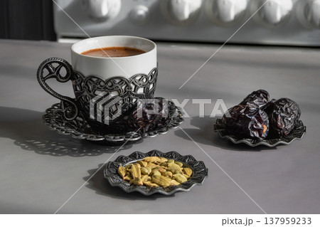 Cup of coffee sits beside dried dates fruits and cardamom seeds. Cup of coffee sits beside dried dates fruits and cardamom seeds. 137959233