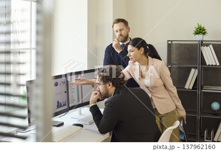 Coworkers reviewing analytics on dual screens during corporate audit meeting Coworkers reviewing analytics on dual screens during corporate audit meeting 137962160