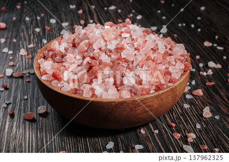 Wooden bowl filled with pink Himalayan salt crystals on dark wooden table, natural mineral seasoning for healthy cooking and spa concepts. 137962325
