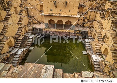Old Indian stepwell with symmetrical stone stairs and murky green water. Old Indian stepwell with symmetrical stone stairs and murky green water. 137962331