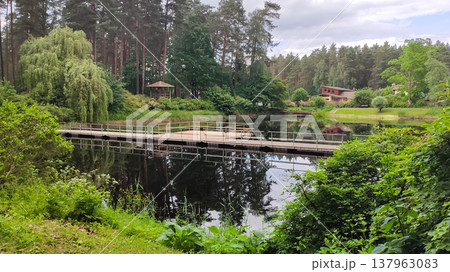 Trees and greenery frame a sunlit pond in the park. A feeling of harmony and leisure. Trees and greenery frame a sunlit pond in the park. A feeling of harmony and leisure. 137963083