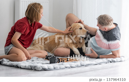Happy Little Girl And Father Play Chess While Petting An Adorable Dog With Happy Family Spending Time Together 137964310