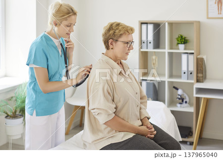 Nurse using stethoscope to examine senior patient during medical clinic visit 137965040