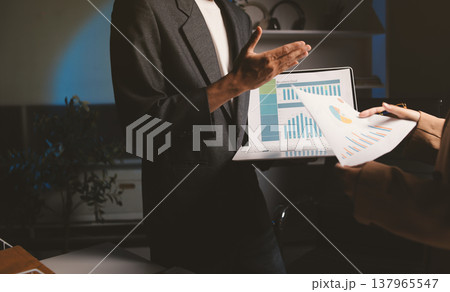 Two business people talk project strategy at office meeting room. Businessman discuss project planning with colleague at modern workplace while having conversation and advice on financial data report. 137965547