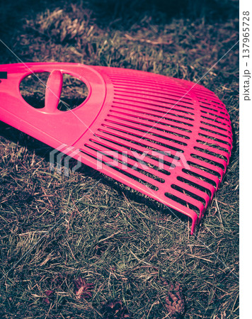 Plastic red rake on ground. Plastic red rake on ground. 137965728