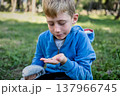 Child exploring nature holding small snail in hand outdoors, curiosity and focus, learning through play 137966745