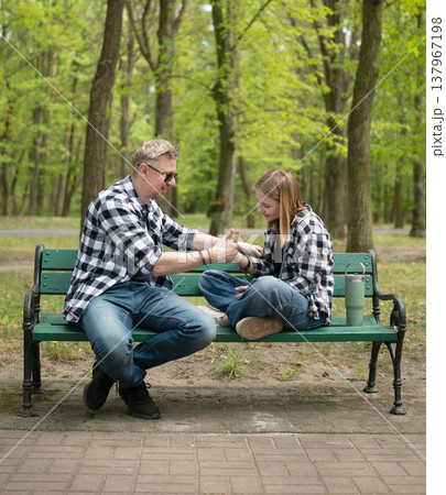 Happy Father And Little Daughter Sitting On A Bench Playing Thumb War Game In Family Look Happy Father And Little Daughter Sitting On A Bench Playing Thumb War Game In Family Look 137967198