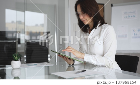 Professional businesswoman in white blouse and glasses attending corporate meeting. Deeply reflecting on business strategy. Making informed decisions. Concentrating on data analysis 137968154
