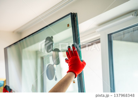 Worker installing new triple glazed window glass unit into frame in apartment interior. Window replacement, home improvement and professional installation process concept. Worker installing new triple glazed window glass unit into frame in apartment interior. Window replacement, home improvement and professional installation process concept. 137968348