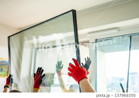 Worker removing one glass panel from triple glazed window unit during disassembly for safe handling and disposal in apartment. Window repair, glass separation and maintenance process concept. 137968350