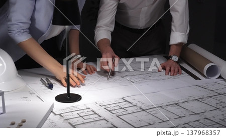 Collaborative team working on an engineering project, reviewing floor plans with a lamp illuminating the architectural drawings. Business and architect people concept 137968357