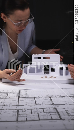 Architects developing a future residential building design, carefully assembling a paper house model on top of blueprints. Concept of architecture and business in low key lighting 137968390