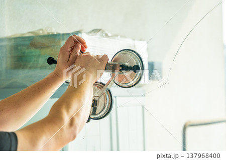 Worker attaching suction cup lifters to cracked window glass before removal from frame during replacement process in apartment. Professional window repair, safe handling, glass installation service 137968400